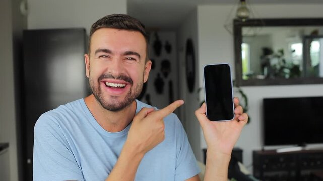 Handsome man showing modern smartphone screen directly on camera after seeing something comedic