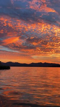 Traditional pavilion overlooking shimmering water at sunset with vibrant orange clouds creating beautiful motion across the sky in this peaceful atmospheric cinematic nature video landscape clip