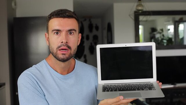 Shocked man opening modern laptop computer and opening his mouth at camera screen while seeing something shocking