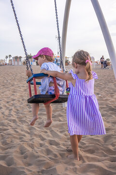 Older sister pushing younger sister on a swing at the beach