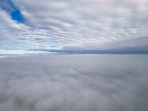 High altitude aerial drone shot flying above a thick fog cover with blue sky and scattered clouds visible overhead.