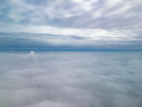 High altitude aerial drone shot flying above a thick fog cover with blue sky and scattered clouds visible overhead.