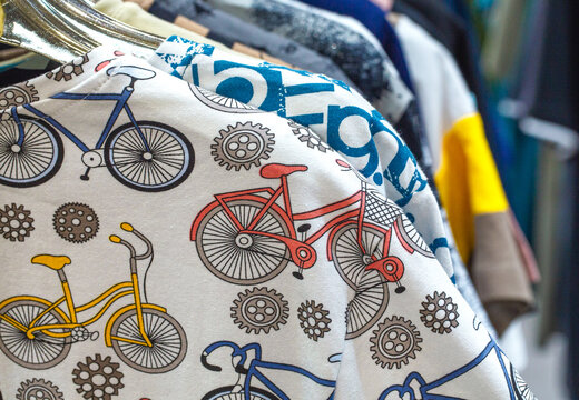 Close-up of colorful bicycle print fabric hanging on a clothing rack, showing patterned garments and textile detail in a retail or wardrobe setting