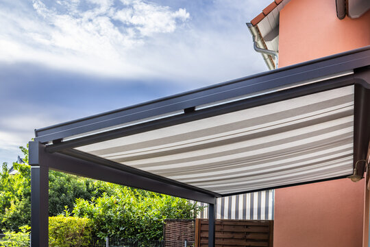 Modern patio pergola with retractable striped awning providing shade on a sunny day