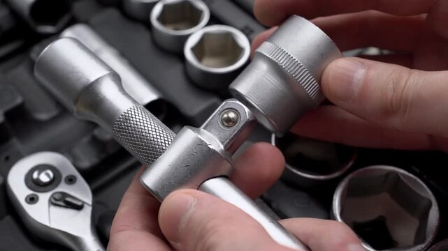 Mechanic hands attaching drive socket head to sliding T-bar extension handle close-up in workshop background