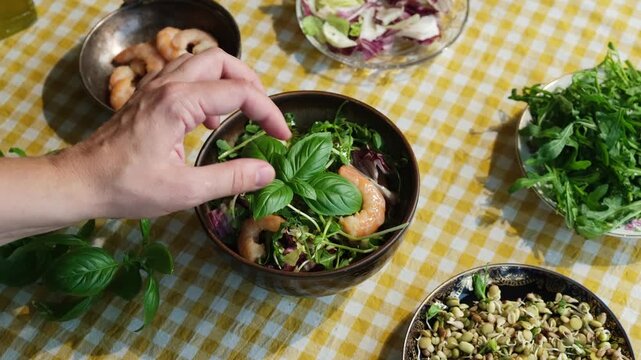 Cooking seasonal summer salad with shrimp and greens. Hand decorating salad with basil leaf. Heathy dinner. Diet cuisine.