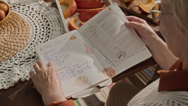 Senior Caucasian woman turning pages of handwritten pumpkin pie recipe book on wooden table with fresh pumpkin slices. Video is perfect for Thanksgiving marketing and autumn cooking tutorials