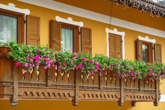 Traditional alpine house featuring a wooden balcony decorated with vibrant pink geranium flowers and rustic shutters