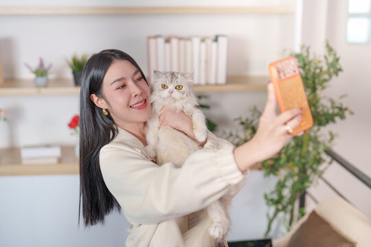 Asian woman taking selfie with fluffy cat on smartphone at home