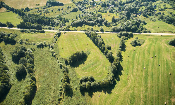 Aerial view of rural landscape with green fields, hay bales, and scattered trees in the countryside of Myadzyel, Minsk Region, Belarus.