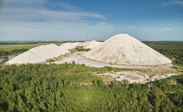 Aerial view of large white industrial mounds of phosphogypsum surrounded by lush green forests and industrial chimneys in the distance in Homiel, Gomel Region, Belarus.