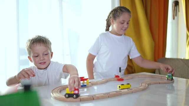 Children play with toy train on railroad. Siblings enjoy fun together in room. Hands moving train wooden tracks. Happy childhood moments as children play with train railroad indoors. playtime in room.