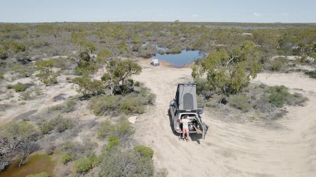 Man Cooking At Rear Of 4WD On Dirt Track In Dry Australian Outback Bushland Aerial Drone Shot