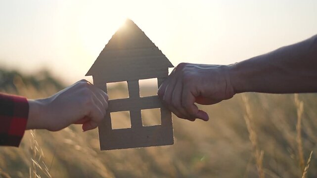 Family holding home cutout at sunset. Silhouette hands symbolizes dream home and unity. Family envisioning future home together. Sunset light creates peaceful silhouette. Family home dream at sunset.