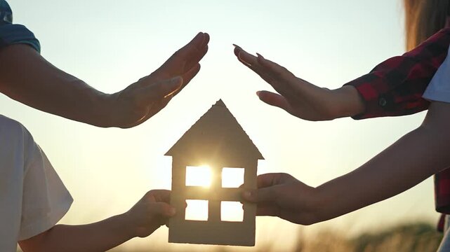 Family holding house cutout symbolizing dream house. Parents children united pursuit real estate. Dream owning house together. Family envisioning future estate investment. House dream real estate.