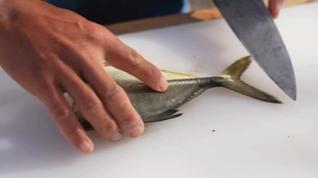 A professional worker uses a sharp knife to clean, slice, and process fresh seafood on a white cutting board aboard a vessel during commercial operations on the open sea