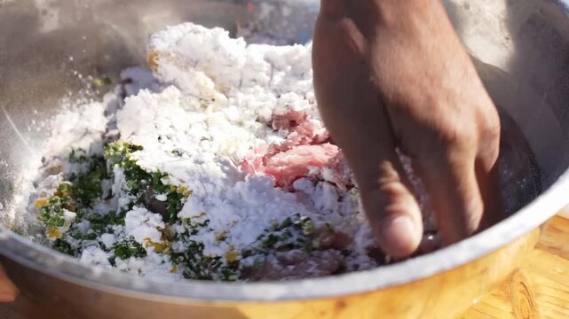 Powdered ingredients fall into a stainless steel bowl containing ground meat and herbs while hands thoroughly combine everything into a cohesive mixture before transferring it into a patterned ceramic