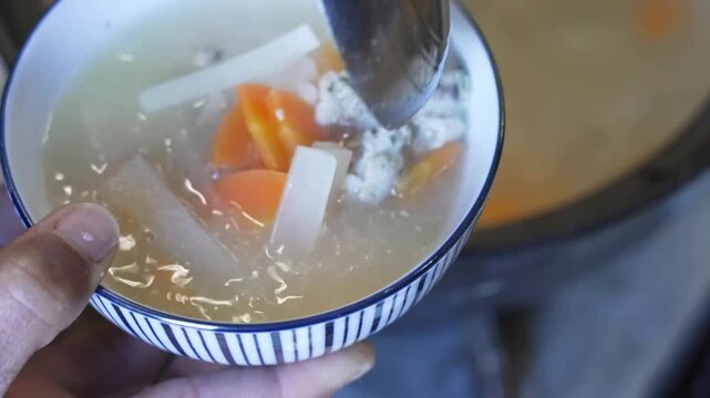 Preparing a hearty meal featuring traditional japanese soup with vegetables, mochi rice cakes, and savory fish balls served in ceramic bowls next to grilled seafood dishes