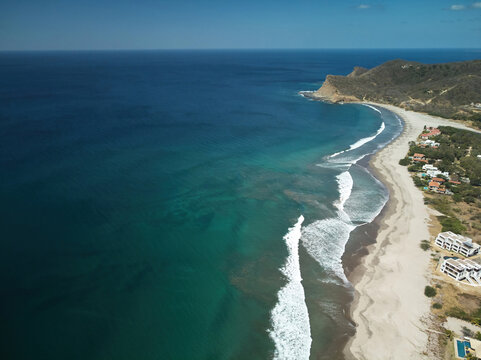 Aerial view of Playa Amarilla with turquoise waves crashing on the sandy beach, coastal vegetation, and modern villas along the shoreline in Tola, Rivas, Nicaragua.