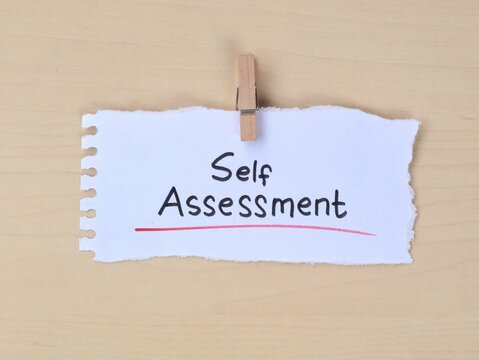 Self Assessment  text handwritten on a torn white piece of paper with a wooden clothespin. Concept for personal development, evaluation, self improvement, business feedback, and career growth