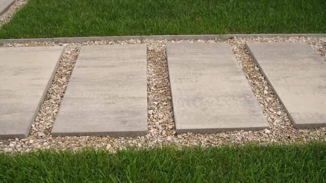 Concrete stepping stones on gravel path beside green grass and paved walkway. Landscape design concept.