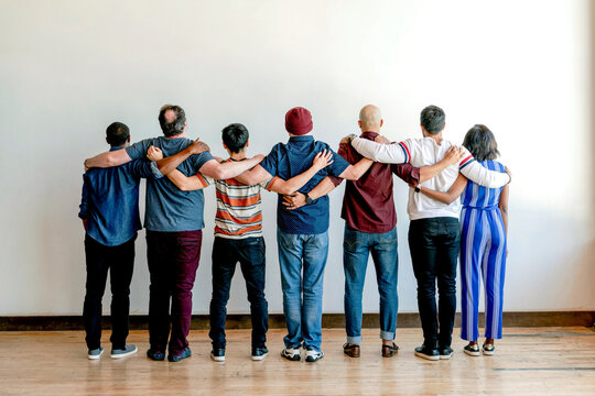 Group of people standing with arms around each other, facing away.