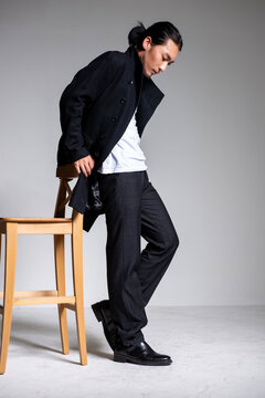 A cool-looking Asian man wearing a black coat was photographed in a studio.
