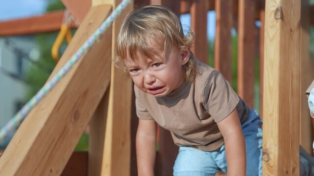Crying child throwing tantrum in park. Emotional child upset during playtime. Child expressing frustration park. Tantrum playground summer light. Crying child upset in park. Toddler tantrum park scene