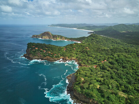 Aerial view of the lush coastline and cliffs of Playa La Redonda with turquoise ocean waves crashing against the rocky shore in Tola, Rivas, Nicaragua.