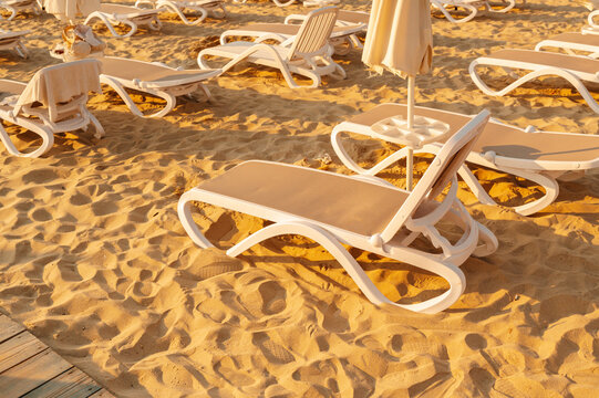 beach lounge chairs arranged on sand with relaxed, serene mood and side view of umbrellas in white and tan.