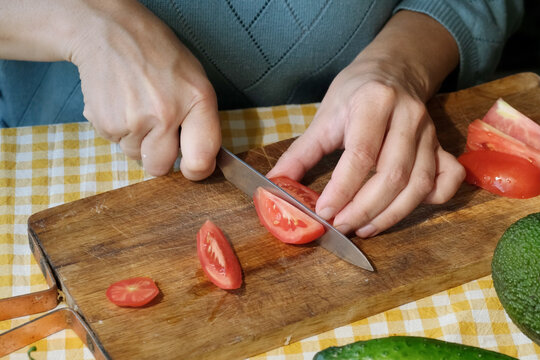 Hands cutting tomato for salad or meal preparation on rustic wooden board. 