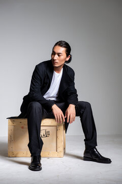 A cool-looking Asian man wearing a black coat was photographed in a studio.
