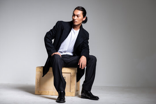 A cool-looking Asian man wearing a black coat was photographed in a studio.