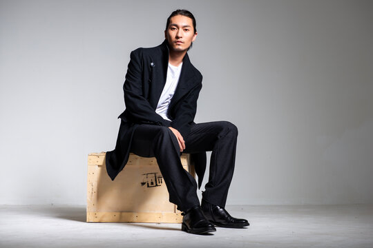 A cool-looking Asian man wearing a black coat was photographed in a studio.