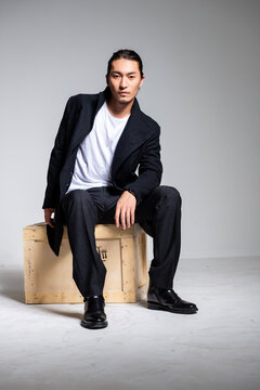 A cool-looking Asian man wearing a black coat was photographed in a studio.