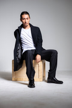 A cool-looking Asian man wearing a black coat was photographed in a studio.