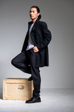 A cool-looking Asian man wearing a black coat was photographed in a studio.
