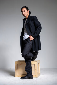A cool-looking Asian man wearing a black coat was photographed in a studio.