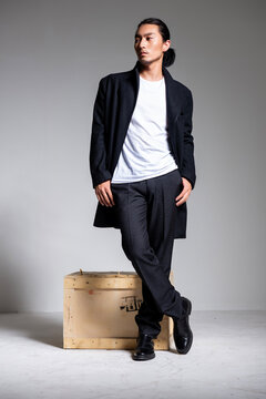 A cool-looking Asian man wearing a black coat was photographed in a studio.