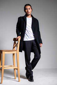 A cool-looking Asian man wearing a black coat was photographed in a studio.