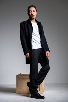 A cool-looking Asian man wearing a black coat was photographed in a studio.