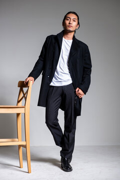 A cool-looking Asian man wearing a black coat was photographed in a studio.
