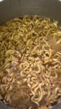 Close up of spicy noodles boiling in a pot at home. Hot bubbling broth and noodles cooking together, capturing a simple homemade meal in preparation.