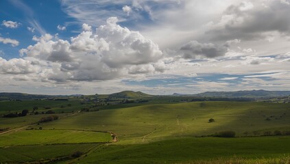 Fototapeta premium Vast Green Rolling Hills Under Dramatic Cloudy Sky in Daylight
