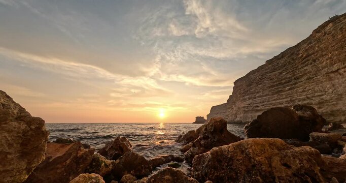 Golden sunset ocean waves wash over dark rugged rocky cliffs at Cape Fiolent. Static low angle shot.