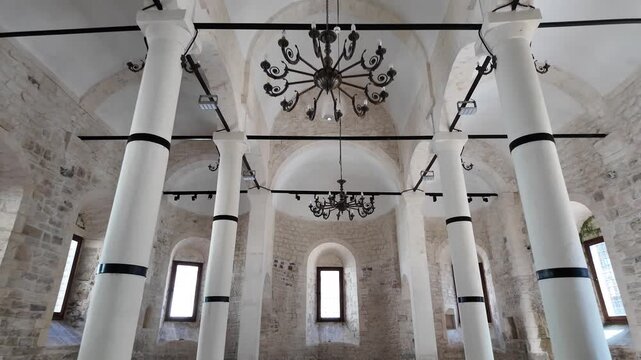 White columns line the spacious, stone-walled interior of the historic Yalı Church in &Uuml;nye, Ordu, featuring arched windows and chandeliers.