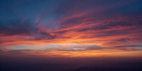 Obraz premium Vibrant Sunset with Colorful Clouds Over a Distant Landscape