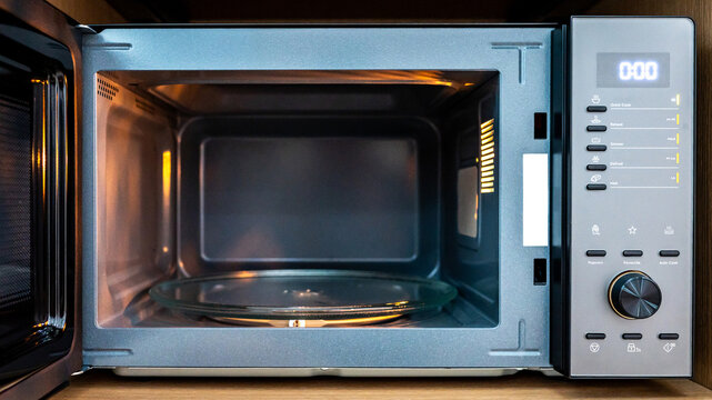 Empty microwave oven with open door. Digital timer display, mode buttons and knob on control panel. Home appliance in the kitchen