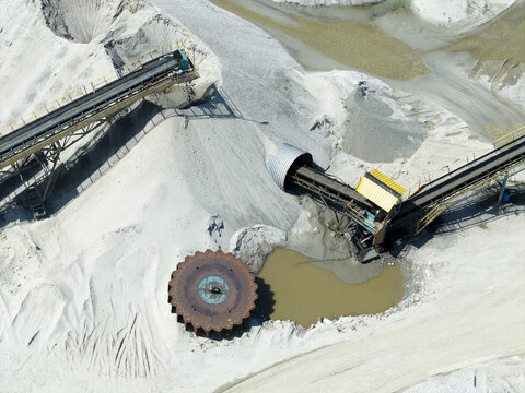 Aerial view of a gravel pit with conveyor belts, heavy machinery, and a large circular gear mechanism near a pool of water in a mining site in Krakow, Lesser Poland Voivode, Poland.