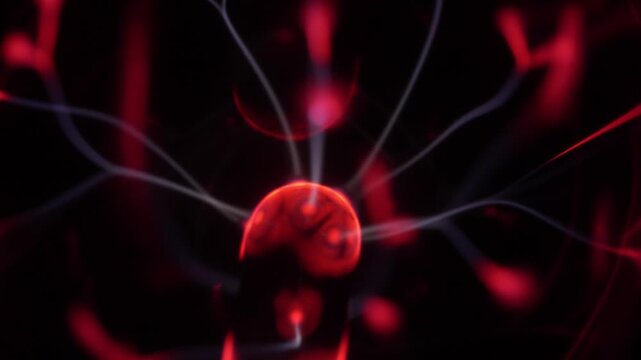 Close-up of a plasma ball coil. The plasma ball creates beams of energy in red and white.